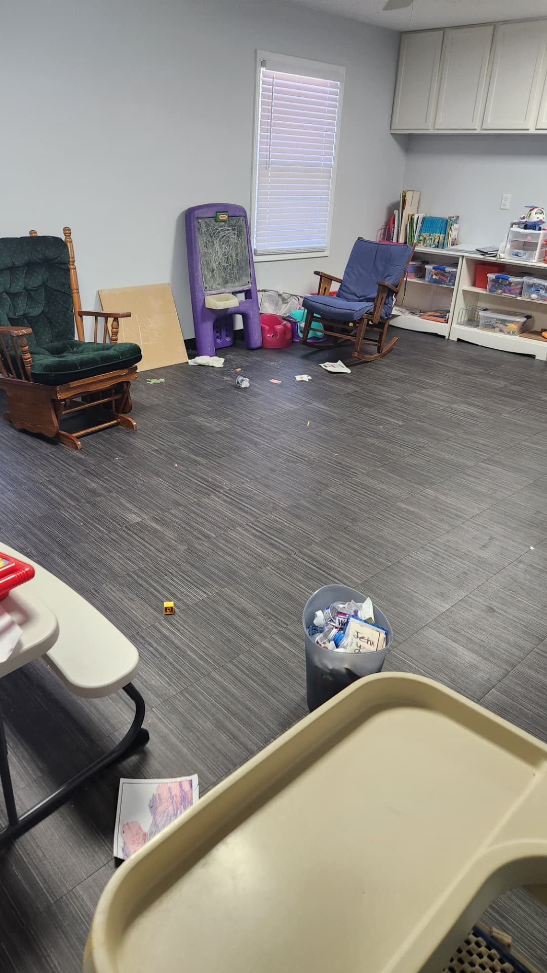 Daycare playroom with litter across the floor and an overflowing trash can before cleaning